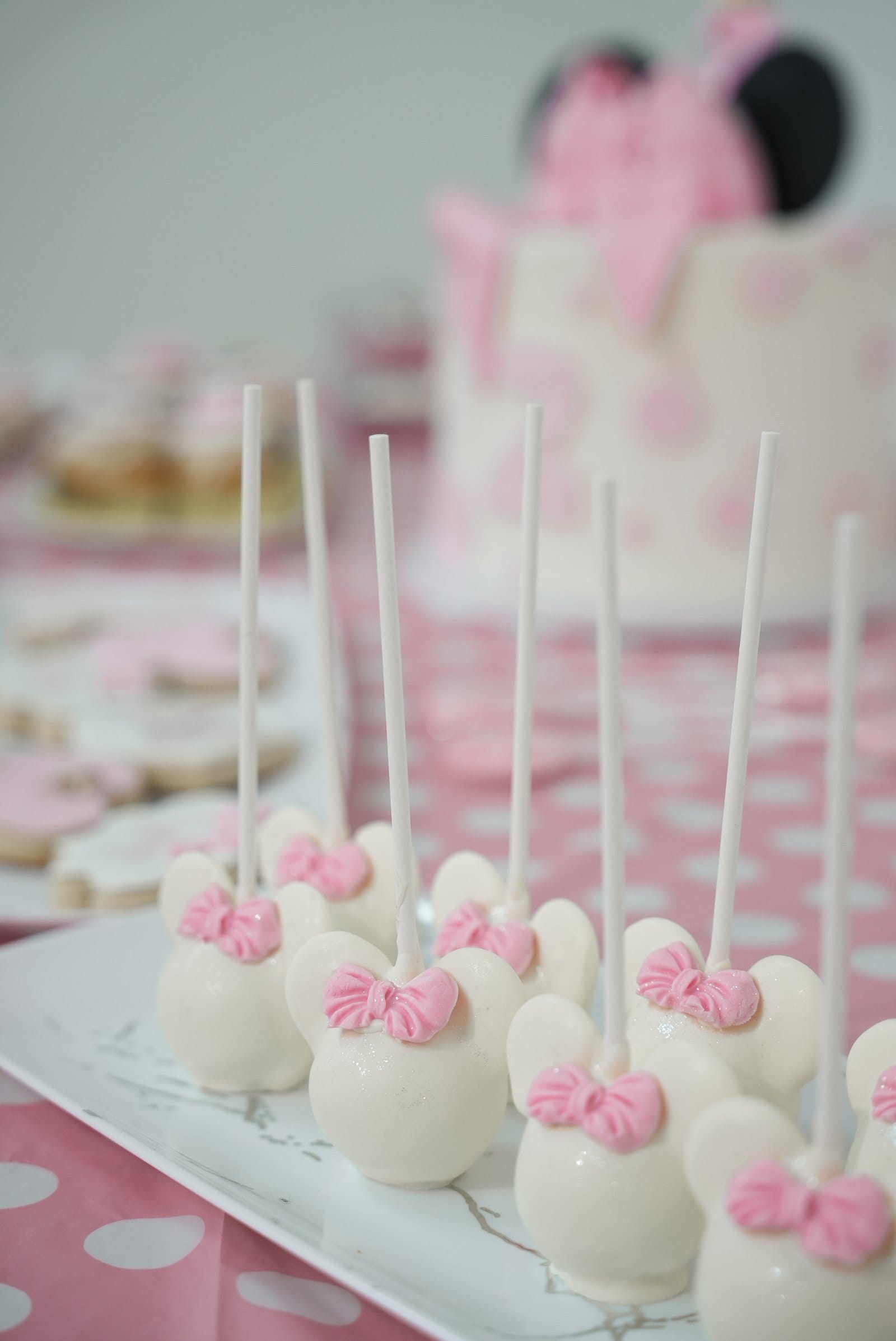 Close-up of a birthday dessert table — Minnie Mouse cake pops with pink bows arranged in front of a decorated cake