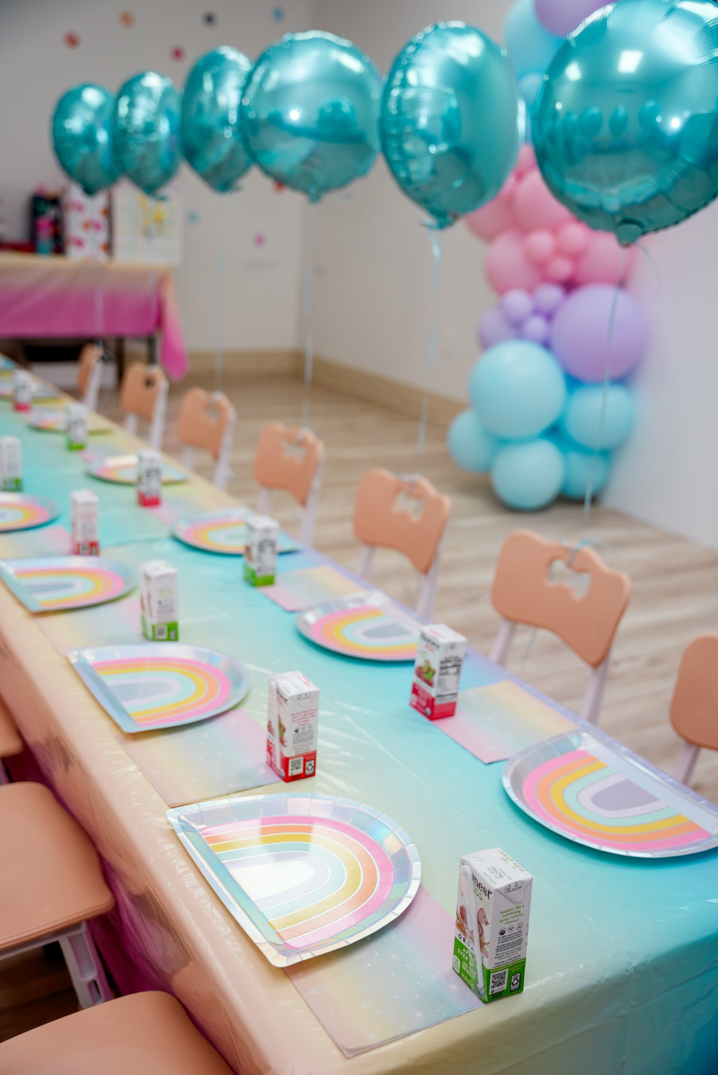 A children's birthday party room set for guests — pastel balloon arch, rainbow plates, and a long table ready for the children to arrive — party photography by Veil & Light in north Jersey