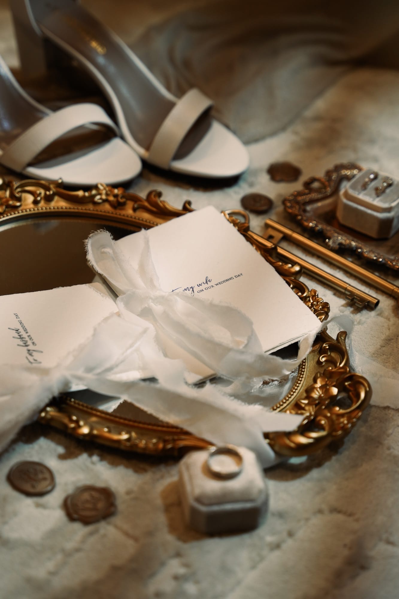Close-up flat lay detail — vow letters on a gold ornate mirror tray with vintage keys and a velvet ring box