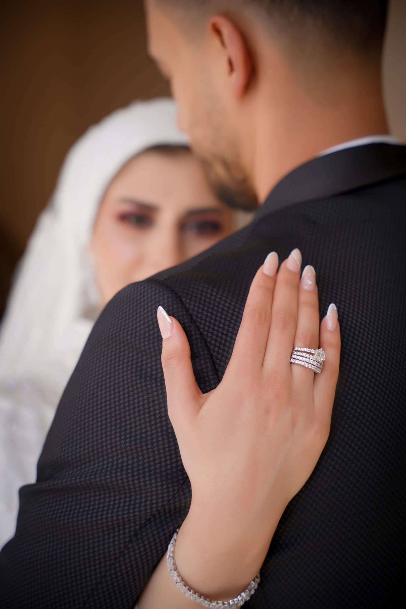 Detail of the bride's manicured hand resting on the groom's shoulder, engagement ring and tennis bracelet in soft natural light