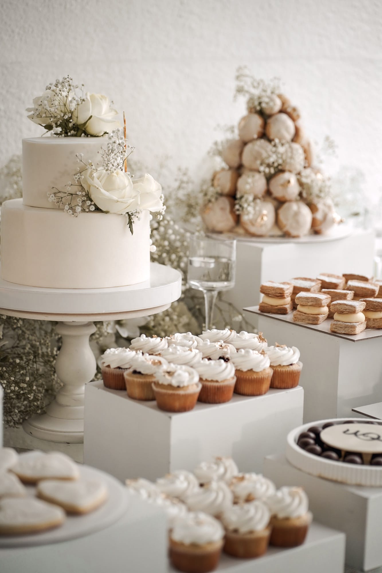 Elegant wedding dessert table — two-tier white cake with garden roses, croquembouche, cupcakes, and macarons