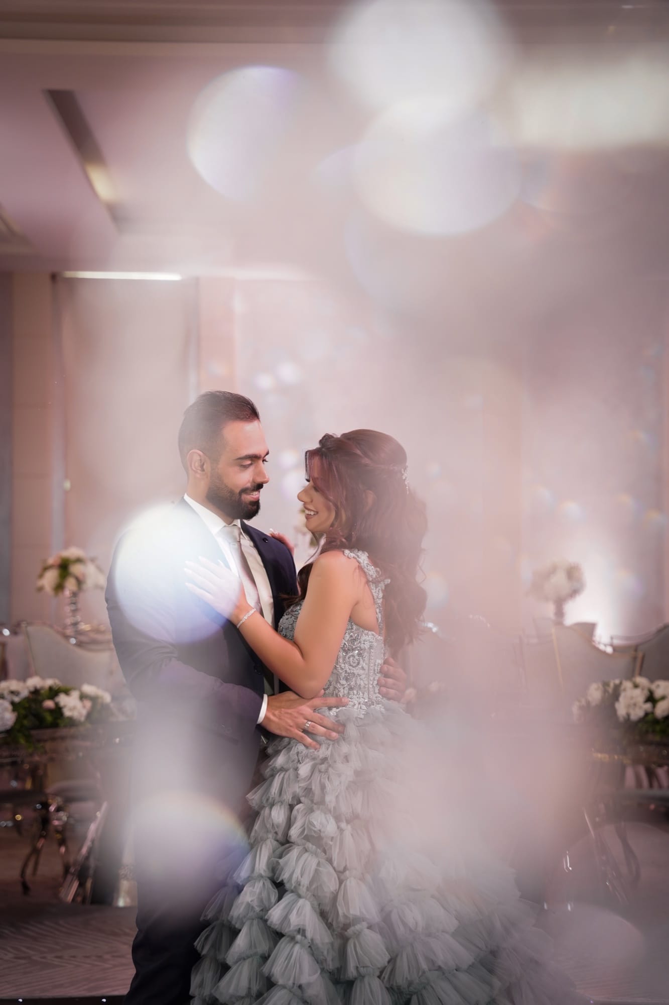Bride and groom slow dancing beneath bokeh ballroom lights at their wedding reception