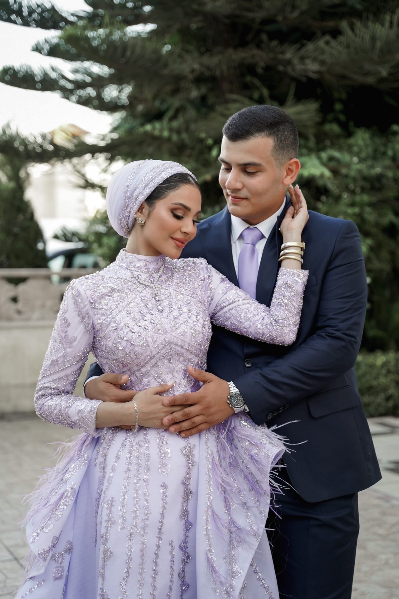 Modest bride in a lavender beaded gown and matching hijab, groom in navy, sharing a tender outdoor moment — modest wedding photography by Veil & Light
