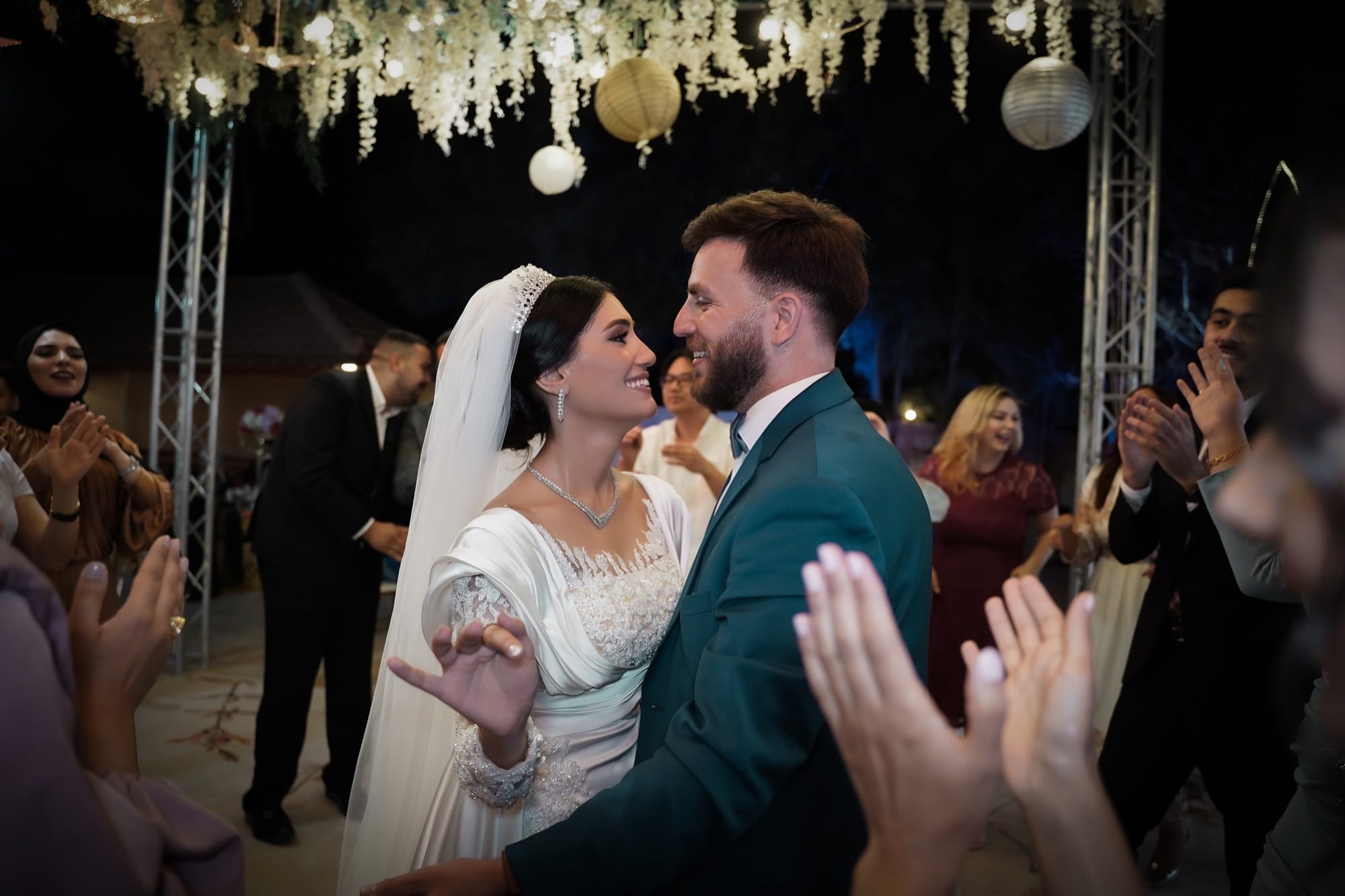 Bride and groom sharing their first dance as guests clap beneath a floral canopy at their wedding reception
