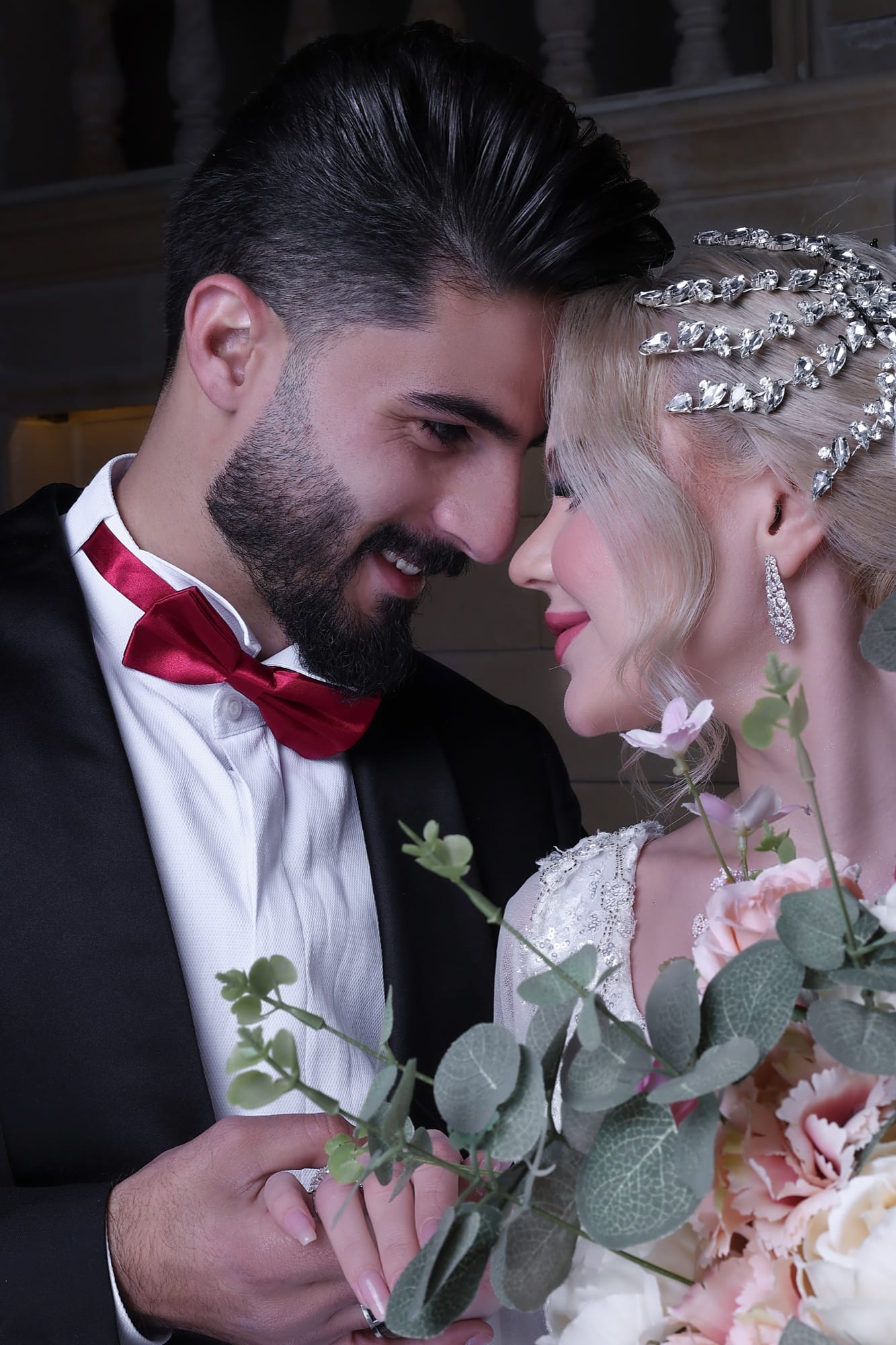 Intimate portrait of bride and groom with foreheads touching, holding a eucalyptus and rose bouquet